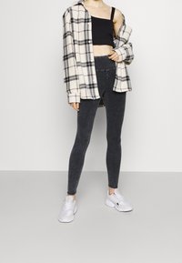 Svarta leggings med hög midja, kombinerade med en oversize plaidskjorta i beige och svart. Avslutat med vita sportskor.