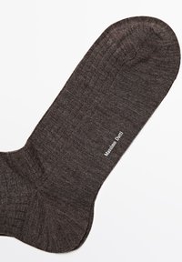 Brąsocka w kolorze brązowym z prążkowaną strukturą. Posiada logo wydrukowane na biało, umieszczone po boku w pobliżu łuku. Okrągły kształt palców.