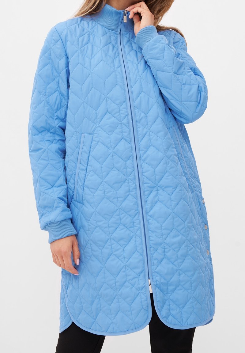 Ljusblå kviltad jacka med hög krage, dragkedja fram och ribbade ärmslut. Har sidofickor och rundad nederkant med tryckknappar.