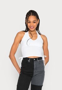 Top cropped branco com alças ajustáveis nas laterais, usado com jeans de cintura alta em tons de preto e cinza. Tecido liso, design ajustado.