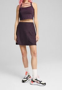 Haut court violet à design à bretelles, associé à une jupe assortie avec un motif texturé. Chaussures : baskets multicolores.