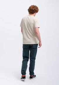 Lichtbeige katoenen t-shirt, ronde hals, korte mouwen, gecombineerd met donkerblauwe tapered broek, met subtiele rode accenten, gedragen met zwarte sneakers.