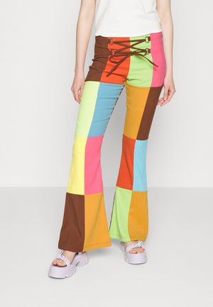 Calças flare coloridas com um design em patchwork com quadrados em rosa, verde, amarelo, castanho, azul e laranja. Inclui um detalhe de laço na cintura.