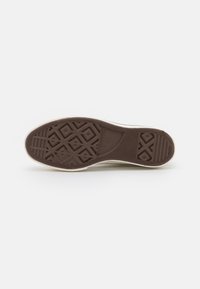 Braune Gummisohle von Sneakern mit einem strukturierten Grip-Muster und einer weißen Kante. Das Design umfasst verschiedene geometrische Formen für besseren Halt.
