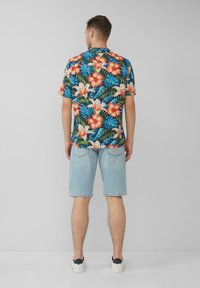 Camicetta a maniche corte con un vivace motivo floreale in rosso, rosa e verde su uno sfondo blu scuro, abbinata a pantaloni corti blu chiaro.