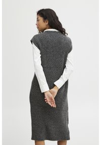 Abito senza maniche grigio a maglia con texture a coste, di lunghezza ginocchio, con spacchi laterali, indossato sopra una camicia bianca con colletto.