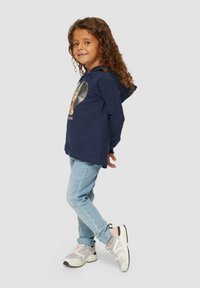 Marineblaues Hoodie mit Vorderseite-Grafik, helle Jeans und mehrfarbige Sneaker. Das Hoodie hat eine Kordel und besteht aus weichem Material.
