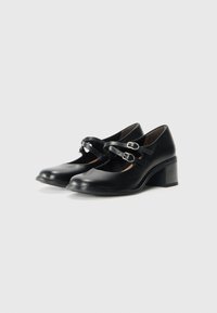 Black leather Mary Jane shoes featuring a rounded toe, two adjustable straps with buckles, and a moderate chunky heel. Smooth texture.