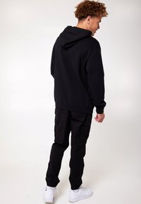 Zwarte hoodie met een relaxte pasvorm, geribde manchetten en buidelzak, gecombineerd met zwarte cargopants en witte sneakers.