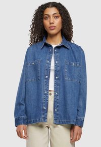 Denim overhemd in een middelblauwe tint, met een knoopsluiting, twee borstzakken en lange mouwen met een ontspannen pasvorm.