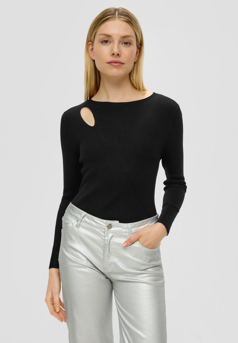 Schwarzer gerippter Pullover mit einem einzigartigen Ausschnitt an der Schulter, kombiniert mit glänzenden silbernen weit geschnittenen Hosen. Sichtbare Nähte und taillierte Designdetails.