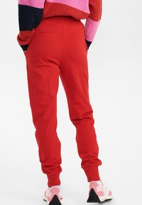 Röda mjukisbyxor i mjukt tyg, med elastisk midja och avsmalnande mudd. Kombineras med rosa och vita sneakers för kontrast.