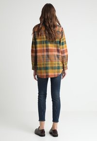 Rutig flanellskjorta i orange, gult, grönt och bruna nyanser. Långa ärmar, knäppning fram och en avslappnad passform. Bärs med mörka jeans och skor.