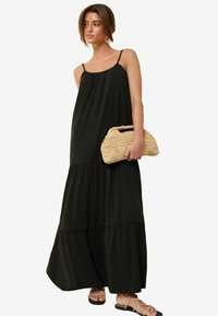 Robe maxi noire avec un design à niveaux, bretelles fines et une texture légère et fluide. Accompagnée d'une pochette tissée beige.