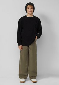 Czarna koszula z długim rękawem z białym kołnierzykiem, luźne oliwkowozielone spodnie i białe trampki z jasnobrązowymi podeszwami. Do tego czarna czapka typu beanie.