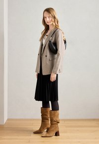 Béžový houndstooth blazer přes bílou halenku, černou plisovanou sukni, černé punčocháče a hnědé semišové boty se slouchy stylem a blokovým podpatkem. Černá kabelka.