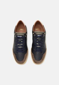 Baskets en cuir bleu marine avec accents en daim, bout perforé, lacets foncés et semelle gomme. Marque visible sur la languette et le talon avec des couleurs contrastantes.