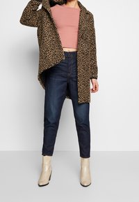 Abrigo de leopardo con mangas largas, combinado con una blusa rosa corta y jeans de color azul oscuro. Botas hasta el tobillo de serpiente beige completan el conjunto.