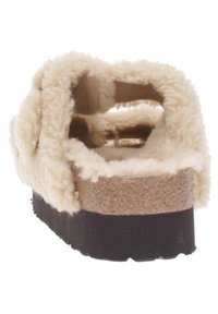 Sandale en mouton beige avec une semelle en liège, dos ouvert, semelle en caoutchouc noire et texture douce sur les bords.