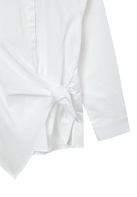 White cotton shirt featuring long sleeves, a tied knot detail at the waist, and a pointed collar. Smooth texture and tailored design.