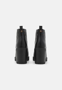 Bottines en cuir noir avec une texture côtelée, talons blocs hauts, et détails de boutons accentués en or à l'arrière pour un enfilage facile.