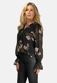 Czarna bluzka w kwiaty z bufiastymi rękawami, z zebranym dekoltem i lekkim, przezroczystym materiałem. W połączeniu z czarnymi dopasowanymi spodniami i złotymi guzikami.