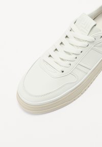 Baskets en cuir blanc avec un bout rond, une languette texturée et un laçage à l'avant. Présentent des rayures latérales minimalistes et une semelle de couleur claire.