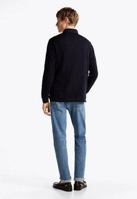 Polo a maniche lunghe blu navy, tessuto morbido, colletto piegato, vista posteriore; abbinato a jeans azzurri chiari, risvoltati all'orlo, scarpe scure.