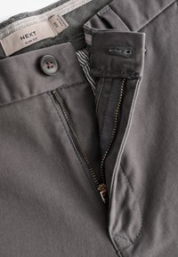 Slim fit dark gray trousers with a zip fly, button closure, and contrasting interior waistband fabric pattern. Textured cotton material.