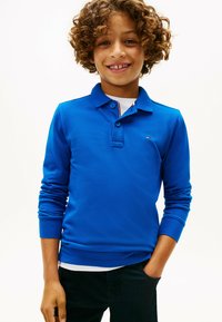 Polo à manches longues bleu avec un col et une patte de boutonnage. Fabriqué en tissu texturé, avec un logo sur la poitrine gauche.