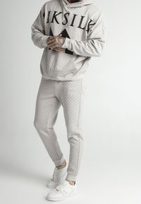 Sudadera gris con patrón y gran texto en negro, combinada con pantalones ajustados a juego. Zapatillas deportivas blancas con detalles de cordones.