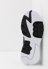 Svart och vit sula på sneakers med texturerade greppmönster, upphöjd profil och "adidas"-logotyp nära hälen.