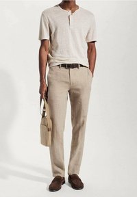 Beige polokošile s krátkým rukávem, světle hnědé lněné kalhoty, hnědý opasek, hnědé nazouvací boty a béžová kabelka přes rameno. Hladká textura, neutrální barvy.