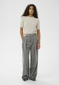 Jasnoszary sweter z krótkim rękawem, w połączeniu z szerokimi spodniami w szare paski z przodu, które mają zaszewki, tworząc zorganizowaną i swobodną sylwetkę.