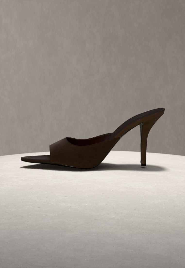 Single dark brown high-heeled mule shoe with pointed toe on a light surface against a neutral gray background.