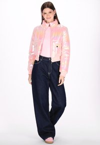 Różowa irydyscentna kurtka puchowa o krótkim kroju z przednimi kieszeniami, w połączeniu z szerokimi dżinsami w ciemnym kolorze i jasnoróżowymi butami.