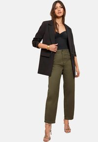 Sort blazer med rullede ærmer, tætsiddende sort top, olivenfarvede vide bukser og sandaler med stropper og slange-mønster.