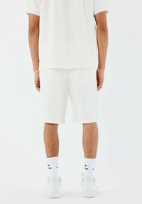 Camisa blanca de manga corta de canalé y pantalones cortos a juego, ambos hechos de un material ligero. Calcetines blancos y zapatillas completan el conjunto.
