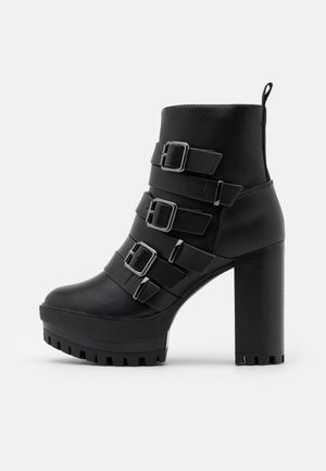 Czarny skórzany botek za kostkę z masywnym wysokim obcasem i platformą, wyposażony w cztery regulowane paski z klamrami oraz pętelkę z tyłu.