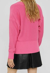 Różowy sweter z dzianiny z prążkowanym wykończeniem u dołu i przy mankietach, charakteryzujący się luźnym krojem i fakturowanymi detalami na rękawach, zestawiony z czarną skórzaną spódnicą.