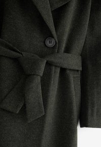Mørkegrøn uldblandingsfrakke med en tekstureret finish, der har en bred krave, lukning med enkel knap og et bælte, der kan bindes i taljen.