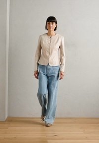 Ljusbeige figursydd läderjacka med dragkedja fram, i kombination med lösa ljusblå jeans och glänsande silverfärgade skor. Släta texturer genomgående.