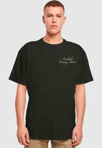 Black cotton t-shirt with short sleeves, featuring white cursive text "Football's Coming Home" on the front. Classic round neckline.