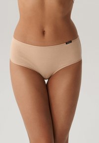 Beżowa bawełniana bielizna hipster w bezszwowym wzorze, średni stan, z czarną metką po lewej stronie. Gładka tekstura.