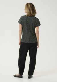 Korte mouwen, donkergroene top met een zebra-patroon, gecombineerd met zwarte, losse broeken en zwarte ballerina's. Glad textuur, casual ontwerp.