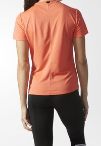 Pomarańczowa koszulka sportowa z krótkim rękawem, o teksturowanej strukturze, z okrągłym dekoltem i pionowym szwem na plecach poprawiającym dopasowanie.