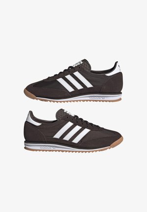Czarne trampki Adidas z białymi paskami, gumową podeszwą i niskim fasonem, pokazane z boku i pod kątem na białym tle.