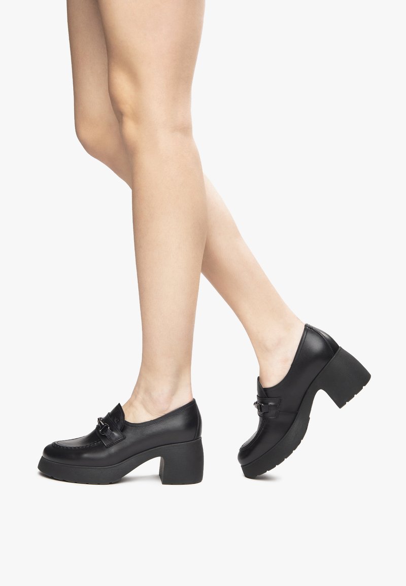 Black leather platform shoes with a rounded toe, featuring a decorative buckle and textured sole. Chunky heel provides substantial height.