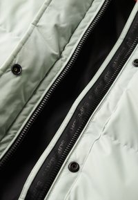 Lysegrøn pufjakke indvendigt med sort foring, med lynlås lukning og trykknapper. Synlige syninger indvendigt.