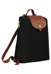 Schwarzer Rucksack mit braunem Lederdeckel, goldfarbenem Reißverschlussgriff und verstellbarem braunem Stofftragegurt, dargestellt auf einem weißen Hintergrund.